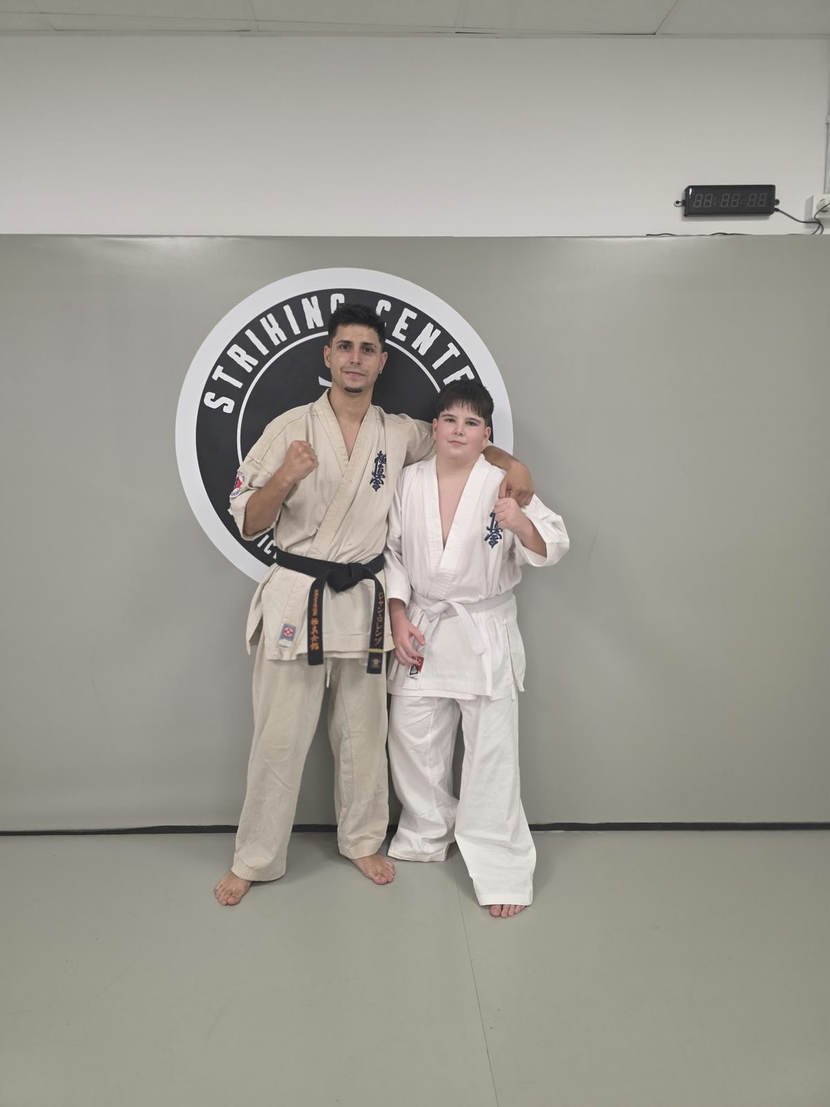 Sensei y alumno juvenil con el puño en alto delante del logo de Striking Center BCN